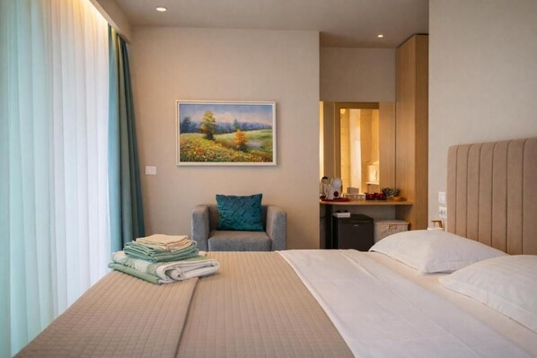 A hotel room with a bed, a chair, a desk, and a painting on the wall.