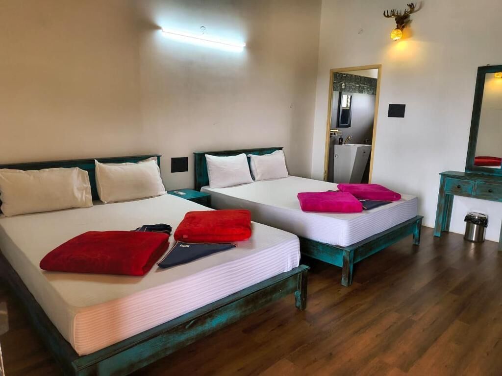 A room with two beds, each with a white mattress and teal headboard. There is a mirror on the wall and a small table with a trash can.