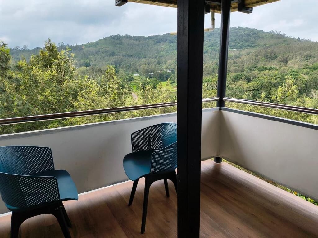 A balcony with two chairs and a view of a forested hillside.