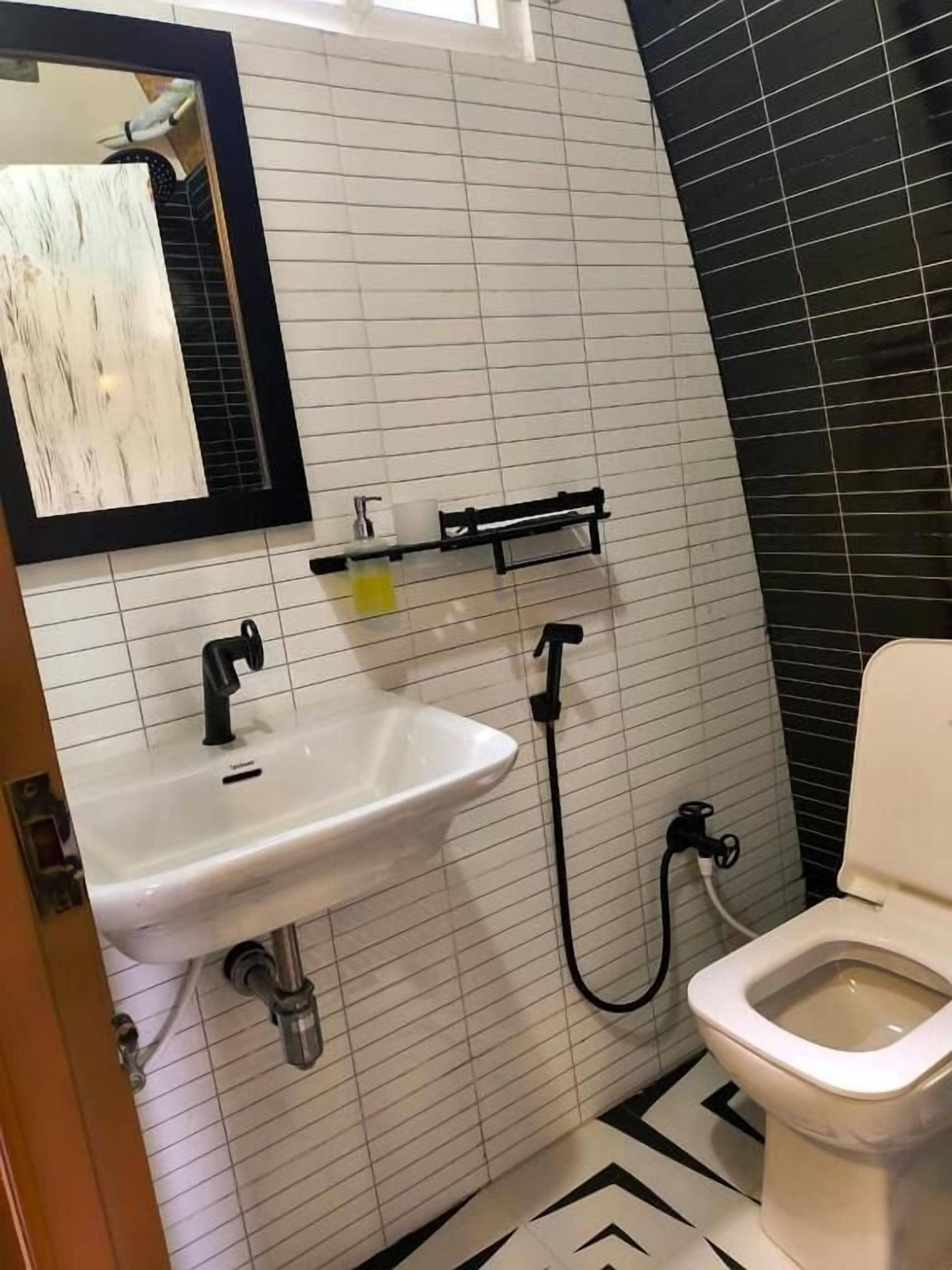 Een badkamer met een wit wastafel, een zwarte kraan en een toilet. Boven het wastafel hangt een spiegel en de muur is betegeld in het zwart.