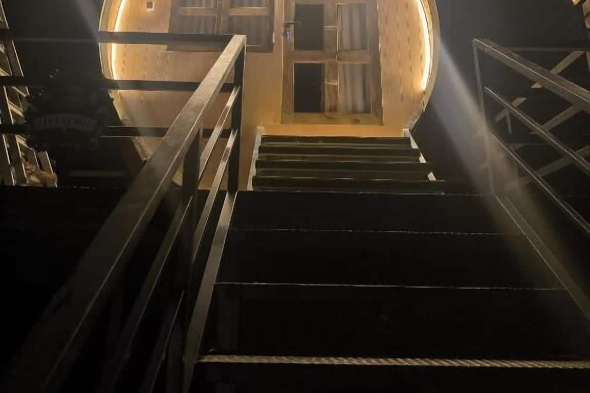 A circular building with a wooden exterior and a glass door, connected to a staircase leading up.