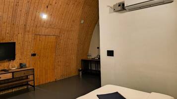 Een kamer met een gebogen houten plafond, een bed met een wit matras, een flatscreen televisie op een houten dressoir en een wandairconditioner.
