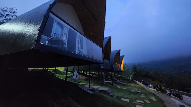 A modern building with a unique curved roof design, large windows, and a grassy area in front. - Gambhiraa Resorts (Kolli Hills)