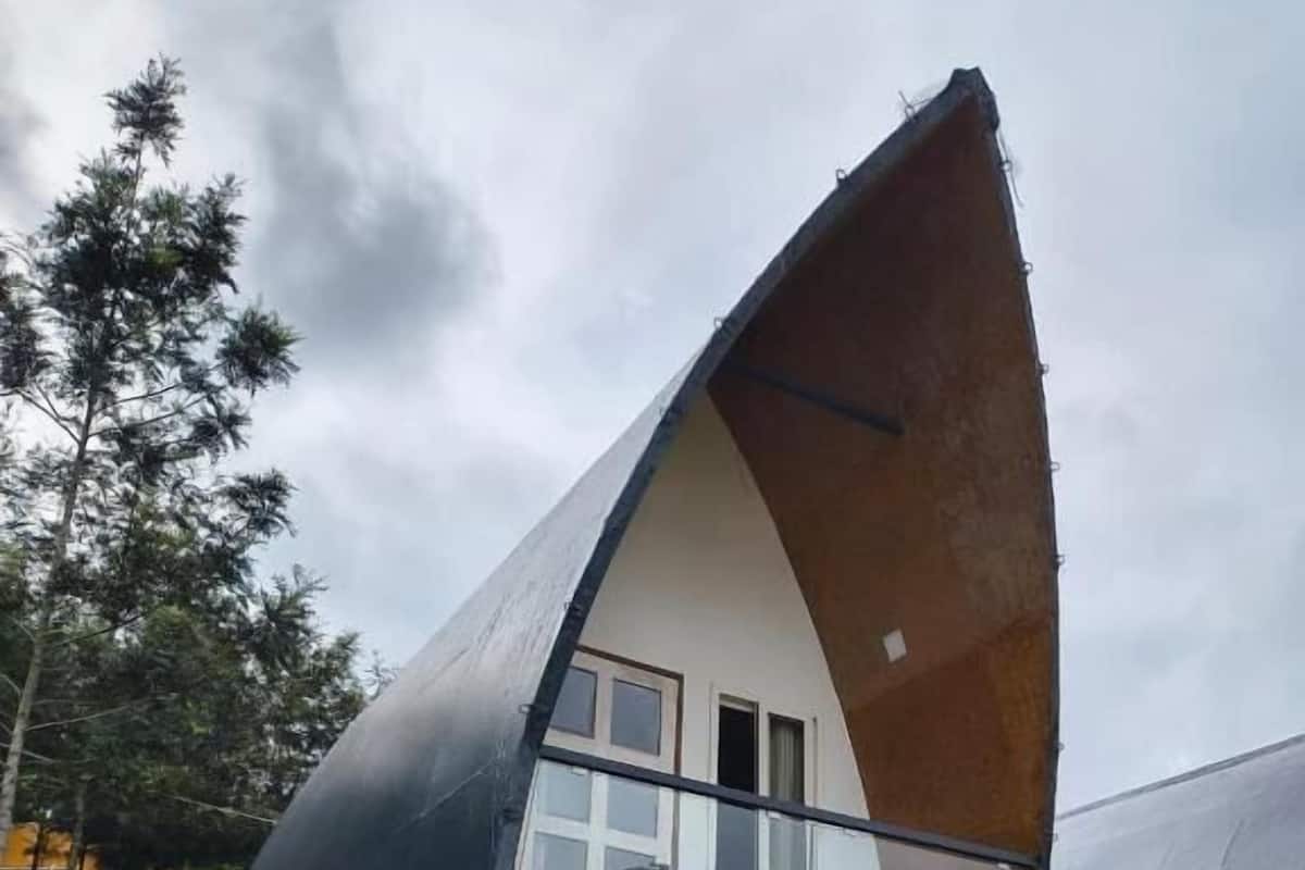 A modern, triangular-shaped building with a flat roof, a balcony with chairs, and a small staircase leading up to the entrance.