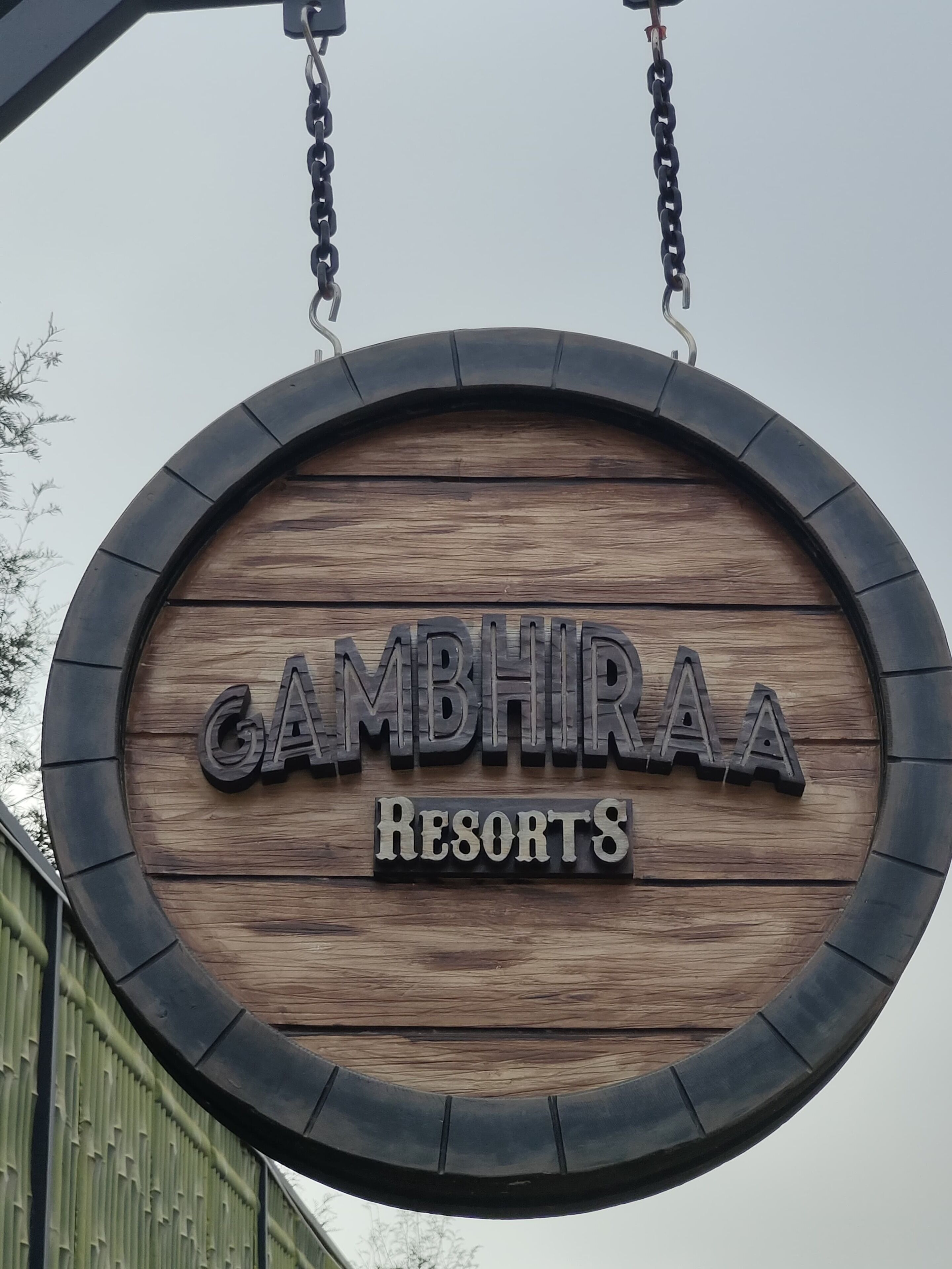 Un cartello di legno con la scritta "GAMBHIRAA Resorts" in caratteri maiuscoli.