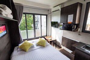 Ein Hotelzimmer mit Bett, Schreibtisch, Fernseher, Mikrowelle und einem Fenster mit Blick auf Grünflächen.