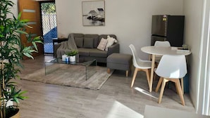 Ein modernes Wohnzimmer mit einem grauen Sofa, einem Glastisch und einem Essbereich mit weißen Stühlen.