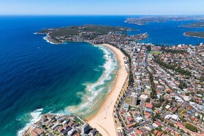 An aerial view of a coastal city with a long beachfront, dense urban area, and a clear blue sea. - Hidden Grove Getaway Kingsgrove (Kingsgrove)
