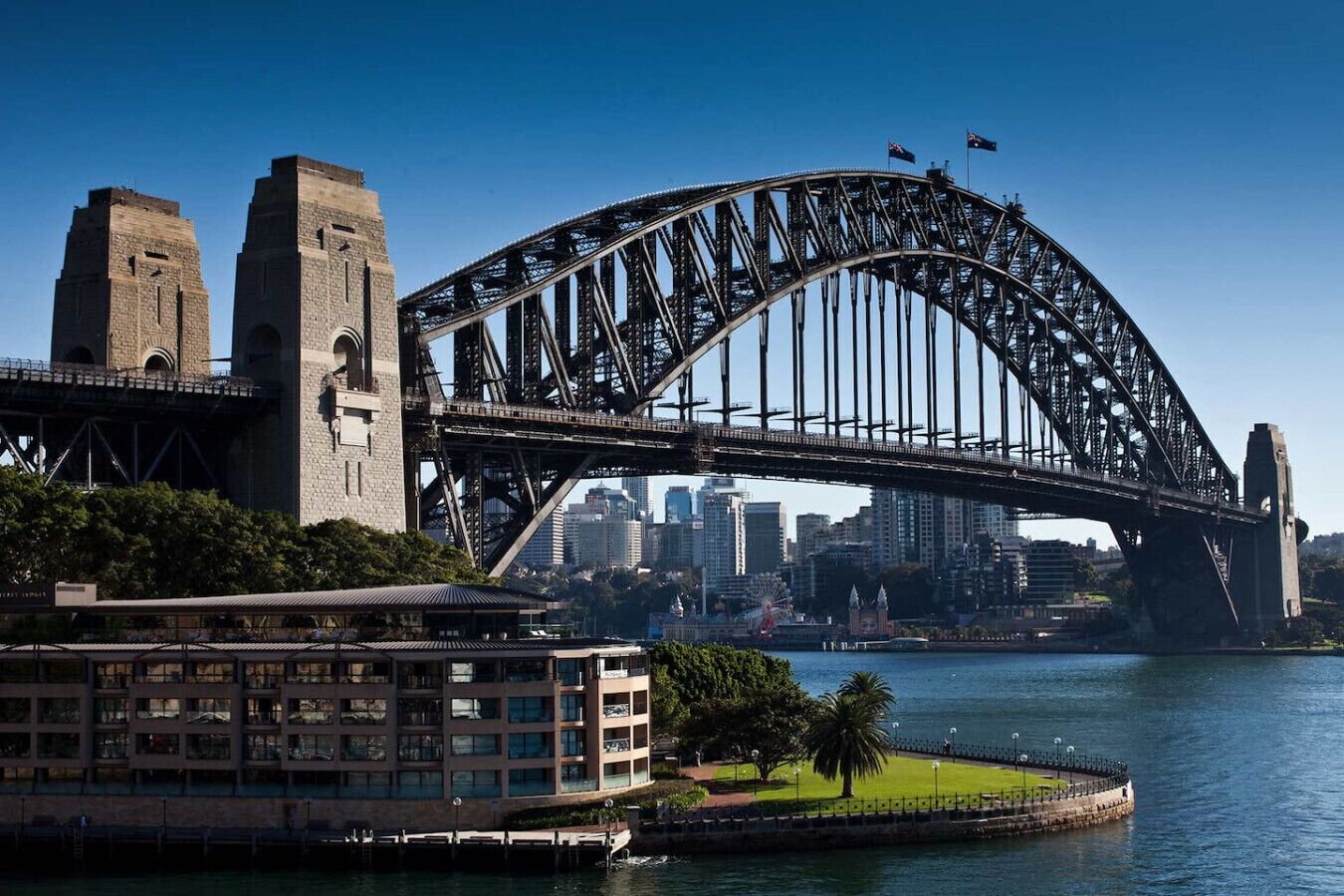Un gran puente de acero que cruza una masa de agua, con el horizonte de una ciudad al fondo.