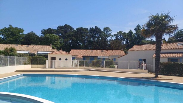 A swimming pool with a tiled deck, surrounded by a fence and a small building with a tiled roof.