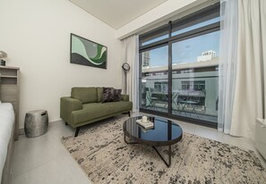 A modern hotel room with a green sofa, a round glass coffee table, a large window with a view of buildings, and a minimalist decor. - Modern Studio in Oxford Boulevard JVC (Dubai)