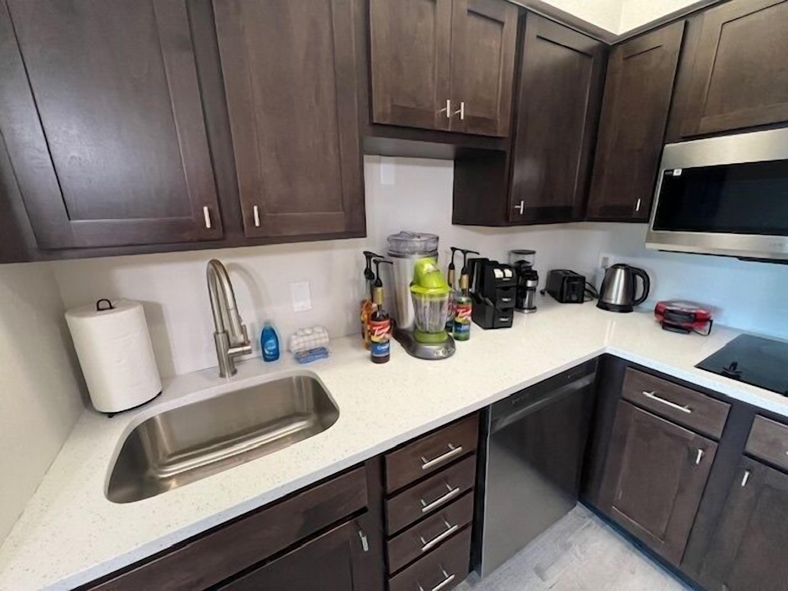 A kitchen with dark wooden cabinets, a stainless steel sink, and various appliances including a coffee maker and a blender.