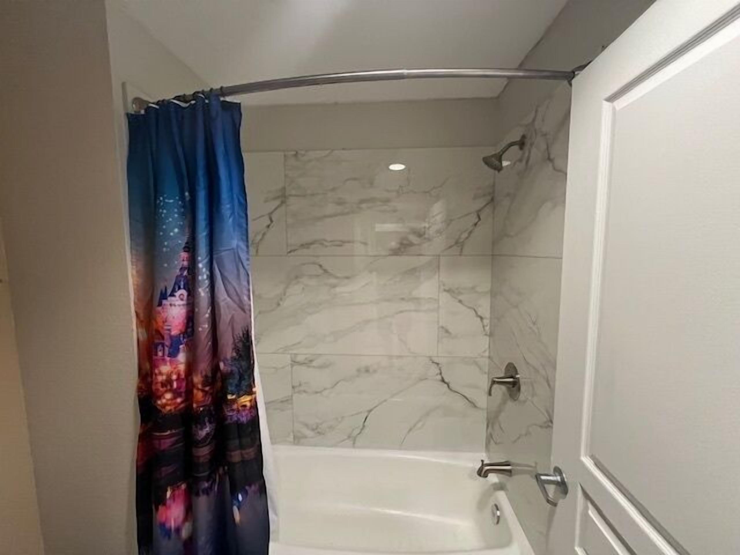A bathroom with a shower curtain featuring a colorful design, a bathtub, and marble walls.