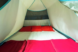 Tienda de campaña con cama en su interior, con un dosel a rayas y ropa de cama roja.