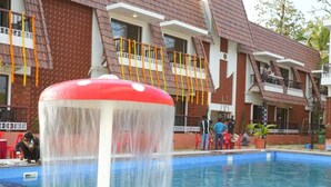 A swimming pool with a water fountain, surrounded by a building with multiple balconies and a tiled roof. - Dandeli River Resort (Dandeli)
