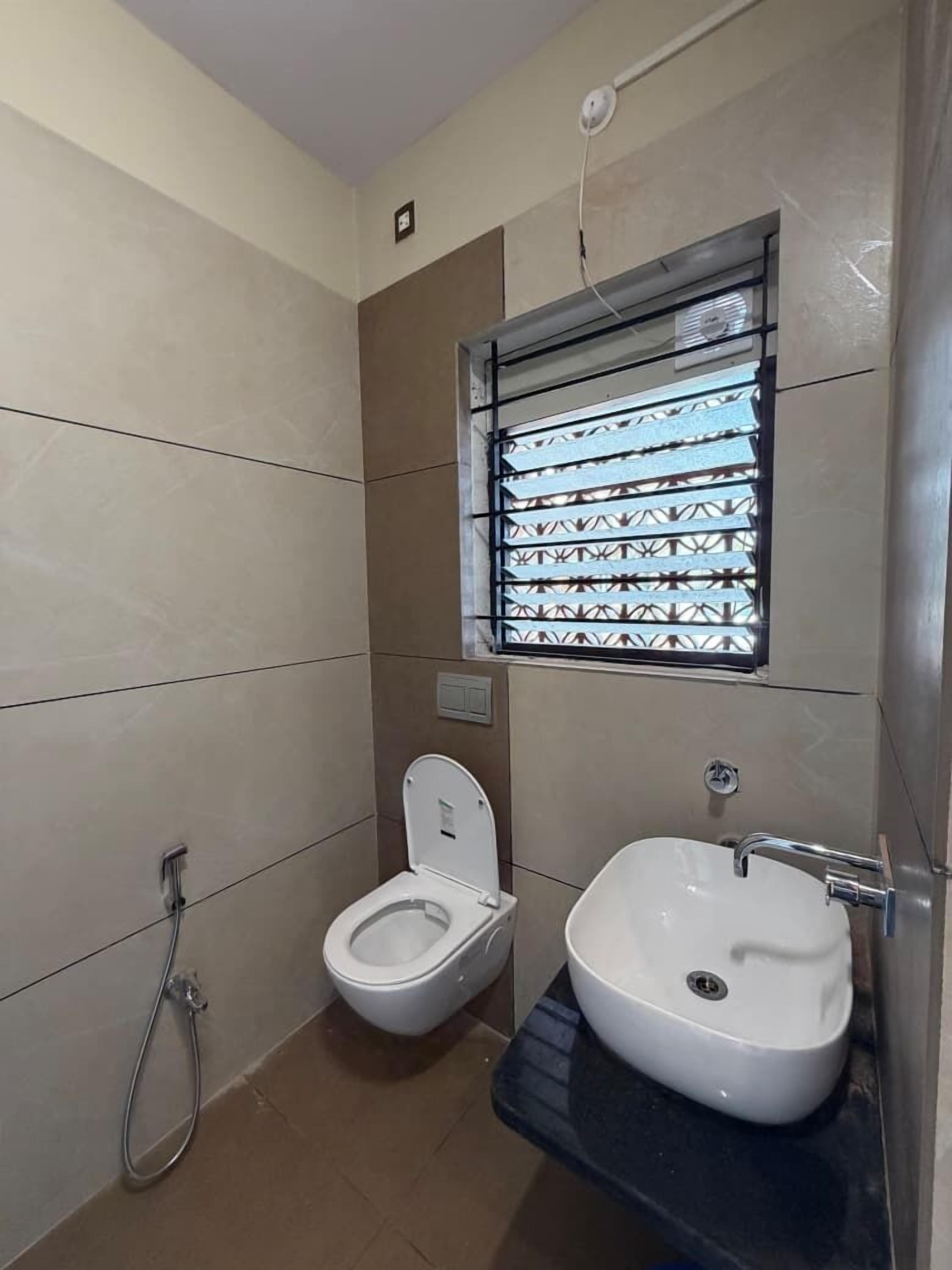 Une petite salle de bain comprenant des toilettes, un lavabo et une fenêtre avec une grille en métal.
