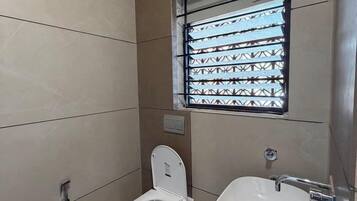 Une petite salle de bain comprenant des toilettes, un lavabo et une fenêtre avec une grille en métal.
