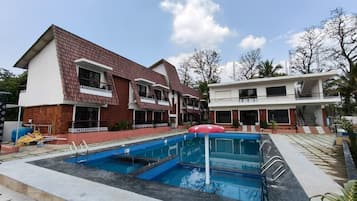 Un edificio residencial con piscina, una sombrilla roja y un balcón.