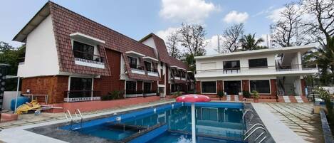 Un edificio residencial con piscina, una sombrilla roja y un balcón.
