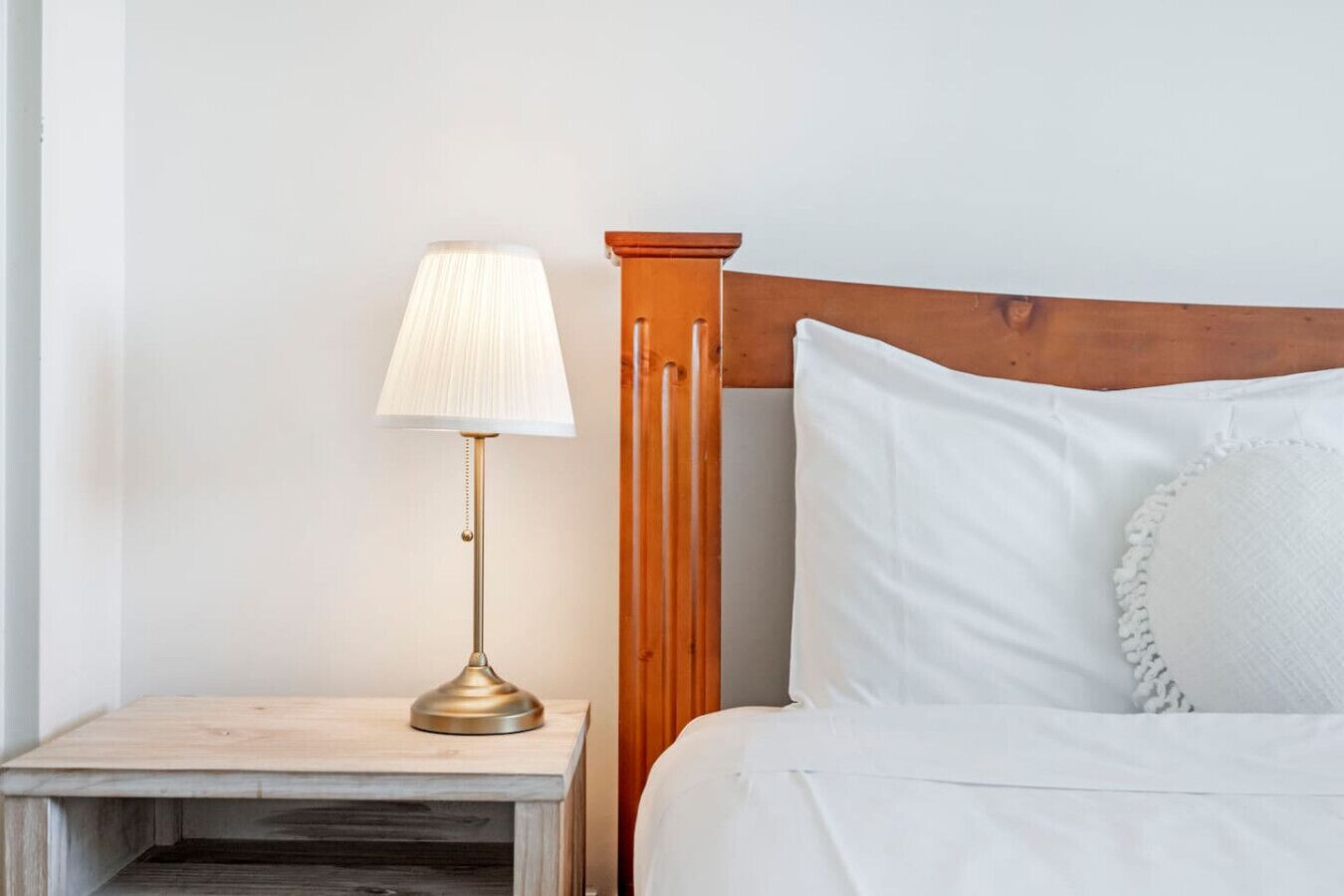 Un lit bien fait, avec du linge de lit blanc et une tête de lit en bois, une petite table de chevet avec une lampe et un mur sobre.