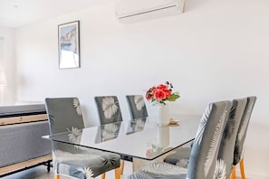 A modern dining area with a glass table surrounded by chairs with leaf patterns, a vase with red flowers, and a framed picture on the wall.