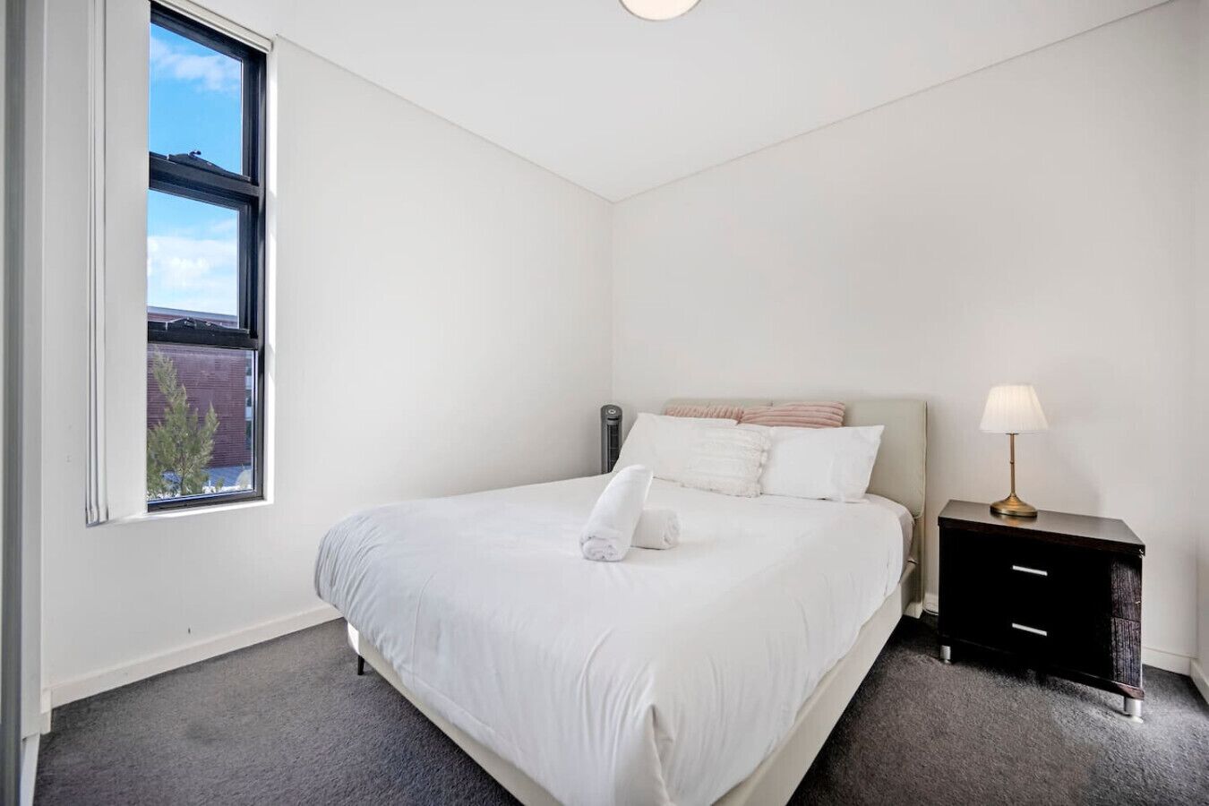 A bedroom with a bed, a nightstand, a lamp, and a window.