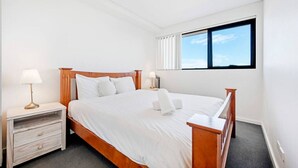 Una camera da letto ordinata con un letto di legno, due comodini con lampade, una grande finestra con persiane e un pavimento tappezzato.