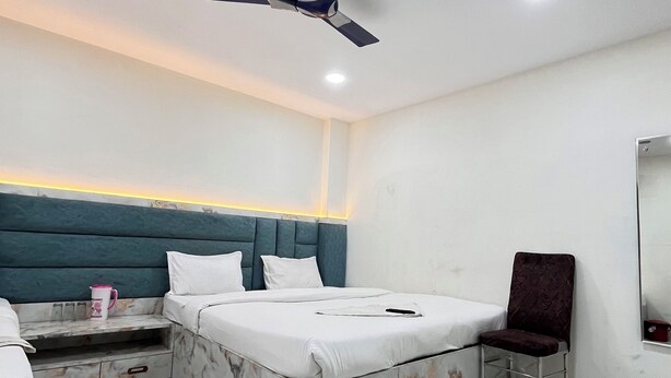 A modern hotel room with a marble-patterned bed, a ceiling fan, and a nightstand with a pink mug. - Sargam Palace (Varanasi)