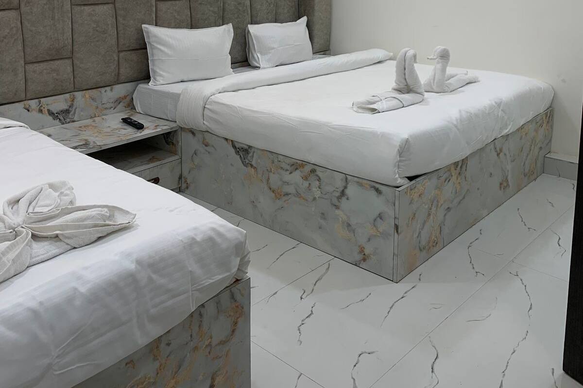 A modern hotel room with two beds, marble-patterned headboards, and a ceiling with recessed lighting.