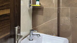 A bathroom with a white sink, a mirror, a shower area, and a wooden door. - Sargam Palace (Varanasi)