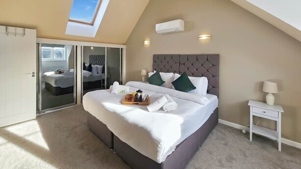 Ein Schlafzimmer mit einem großen Bett, einem Oberlicht, einer Schiebeglastür, einem Nachttisch und einem Beistelltisch.