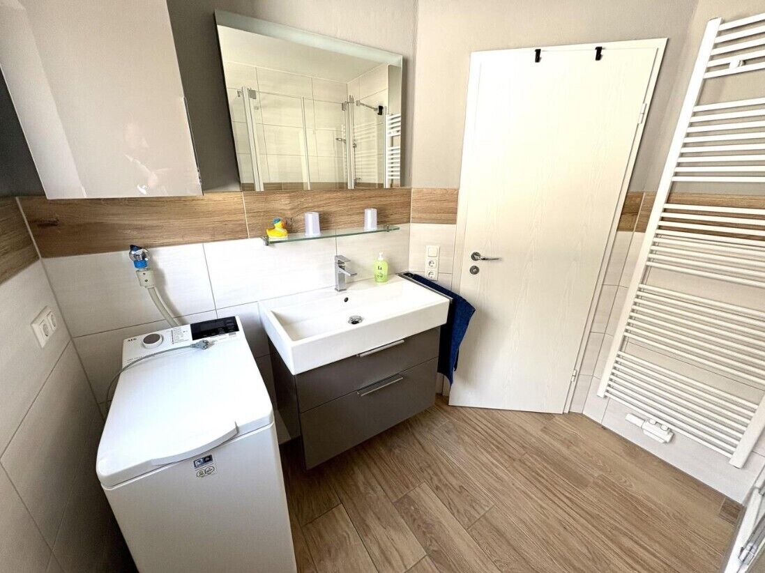 Un baño moderno con lavamanos blanco, espejo y suelo de madera.