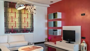 Una sala de estar moderna con un sofá blanco, una mesa de centro redonda, un televisor de pantalla plana y una pared de acento roja.