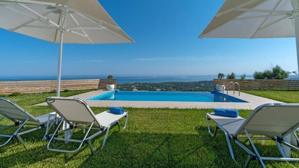 Zona de piscina con dos sombrillas, dos sillas de descanso y vista al océano.