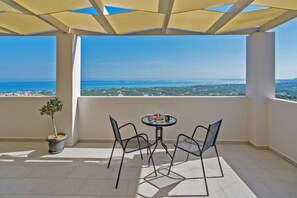A balcony with a table and chairs, a potted plant, and a view of the sea and cityscape. - Alkistis Villa with amazing sea view (9G4V+4G2 Rethymno, Greece)