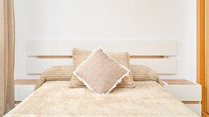 A bed with a white headboard, a beige blanket, and two pillows.