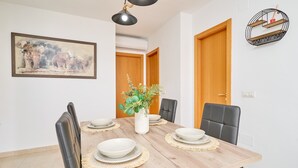 A dining room with a wooden table, black chairs, a white vase with flowers, and a painting on the wall.