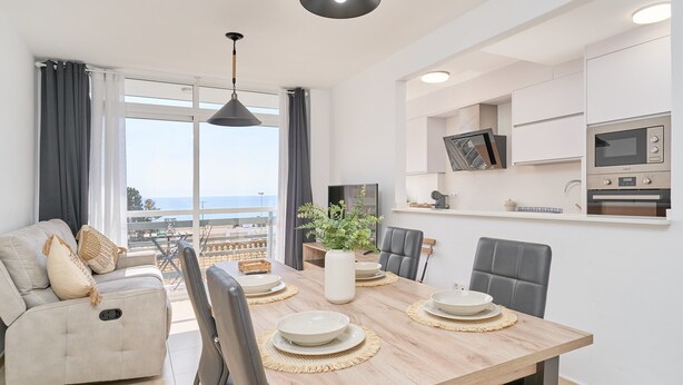 A modern dining area with a wooden table, chairs, a sofa, and a view of the outdoors.