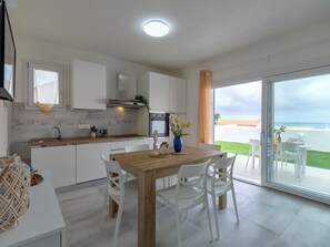 Eine moderne Küche mit weißen Schränken, einem Holzespeisetisch und Meerblick durch große Glasüren.