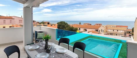 Un balcón con una mesa dispuesta para dos, con vistas a una piscina y al mar.