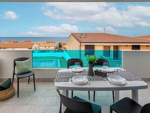 Eine Terrasse mit Tisch für zwei Personen mit Blick auf einen Pool und die Küste.