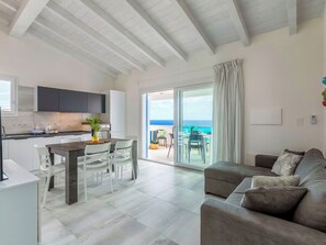 A modern living room with a grey sofa, a dining area with a table and chairs, a kitchen with dark cabinets, and a balcony with a view of the sea. - Cosy apartment for 5 guests with pool, WIFI, A/C, TV, patio and pets allowed (Valledoria)