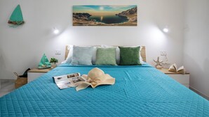 Ein Schlafzimmer mit einem großen Bett, einem Gemälde einer K üstenlandschaft und einem kleinen Tisch mit einem Buch und einer Pflanze.