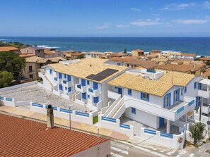A coastal residential area with white buildings, some with blue accents, and a view of the sea. - Nice apartment for 5 guests with A/C, WIFI, pool, TV, patio and pets allowed (Valledoria)