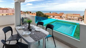 Ein Balkon mit einem Tisch für zwei Personen, mit Blick auf einen Swimmingpool und die Küste.