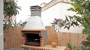Un forno esterno in mattoni con un camino, posizionato su una piattaforma in cemento con una panchina e due vasi verdi.
