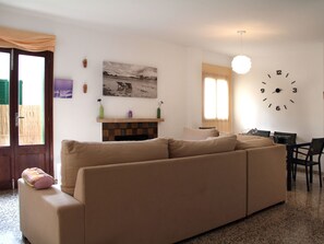 Ett vardagsrum med en beige soffa, en öppen spis, en klocka och en matplats med stolar och ett bord.