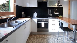 Una cucina compatta con mobili bianchi, un lavello in acciaio inossidabile, un fornello e un piano di lavoro nero.