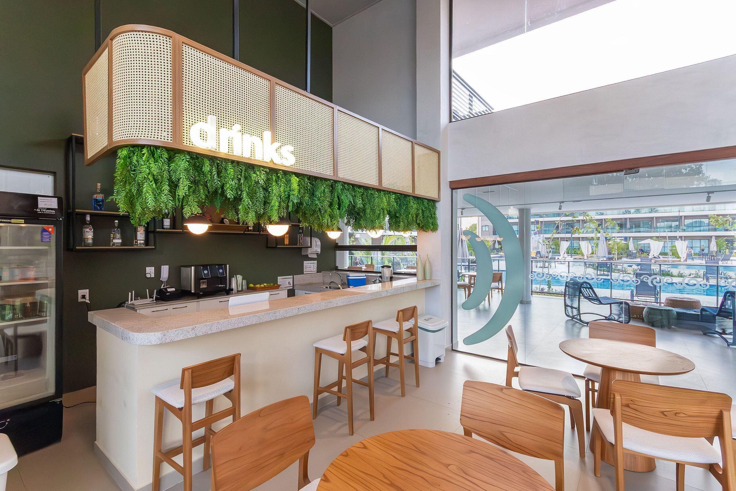 Uma área de bar moderna com um letreiro 'drinks', banquetas de madeira e vista para a piscina.