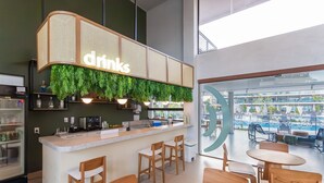 A modern bar area with a 'drinks' sign, wooden bar stools, and a view of the pool outside. - Malia Beach #a301 - Resort por Carpediem (Ipojuca)